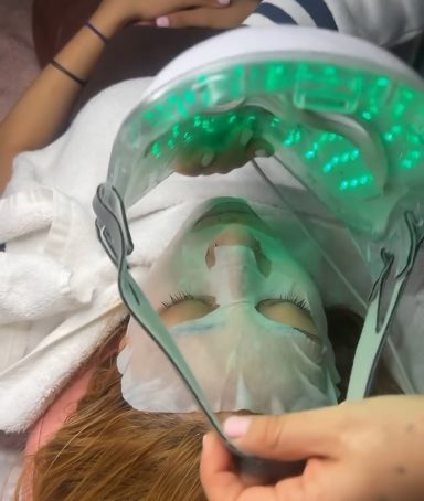 A person receiving a facial treatment with a green light therapy mask.
