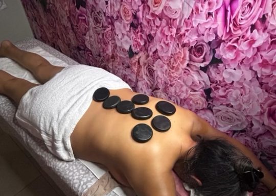 Person lying face down with hot stones placed on their back, surrounded by floral decor.